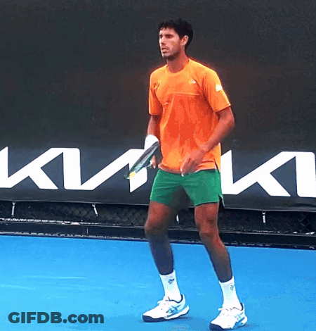 A Man In An Orange Shirt Is Holding A Tennis Racquet GIF