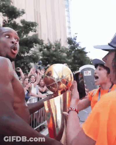 A Man In An Orange Shirt Is Holding A Trophy In Front Of A Crowd Of People GIF