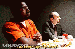 A Man In An Orange Shirt Is Sitting At A Table Talking To Another Man GIF