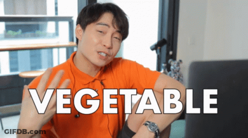 A Man In An Orange Shirt Is Sitting In Front Of A Laptop With The Word Vegetable On The Screen GIF