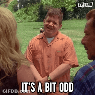 A Man In An Orange Shirt Is Standing In A Park Talking To A Group Of People And Laughing . GIF