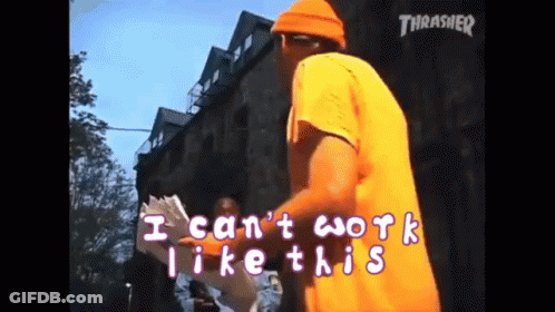A Man In An Orange Shirt Is Standing In Front Of A Building With The Words " I Can 'T Work Like This " Written On It GIF