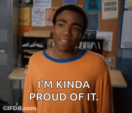 A Man In An Orange Shirt Is Standing In Front Of A Desk And Smiling . GIF