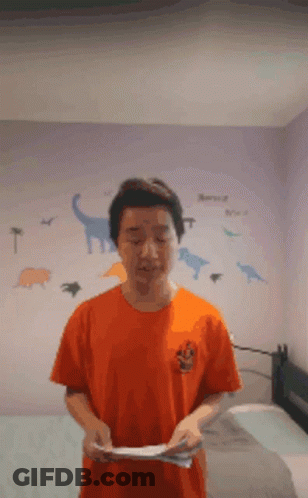 A Man In An Orange Shirt Is Standing In Front Of A Dinosaur Wall Decal GIF