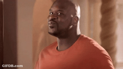 A Man In An Orange Shirt Is Standing In Front Of A Mirror And Making A Funny Face . GIF