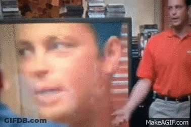 A Man In An Orange Shirt Is Standing In Front Of A Screen With A Picture Of A Man 'S Face On It .. GIF
