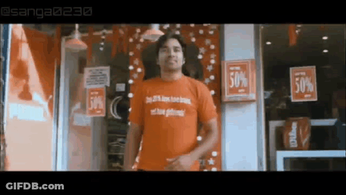 A Man In An Orange Shirt Is Standing In Front Of A Store With A Sign That Says 50 % Off . GIF