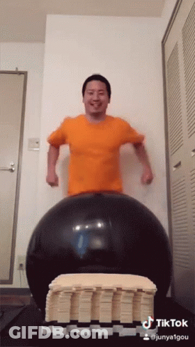 A Man In An Orange Shirt Is Standing On A Large Black Ball With A Tiktok Watermark GIF