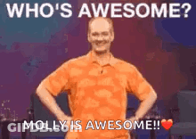 A Man In An Orange Shirt Is Standing On A Stage With His Hands On His Hips And A Heart . GIF