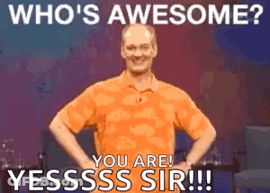 A Man In An Orange Shirt Is Standing With His Hands On His Hips And Says Who 'S Awesome ? GIF