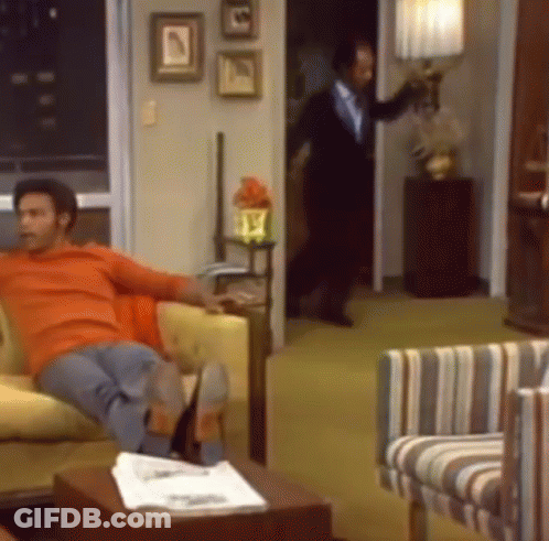 A Man In An Orange Shirt Sits On A Couch In A Living Room GIF