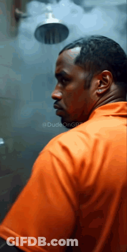 A Man In An Orange Shirt Stands In Front Of A Shower GIF