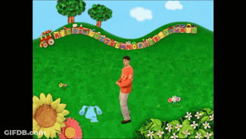 A Man In An Orange Shirt Stands In Front Of A Train With The Letters Abcdefghijklmn On It GIF