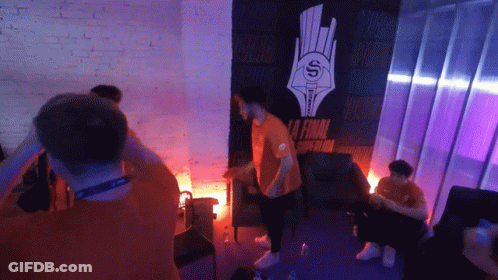 A Man In An Orange Shirt Stands In Front Of A Wall That Says La Final GIF