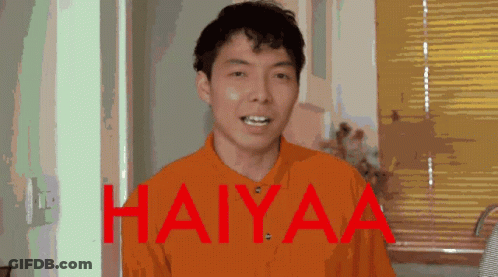 A Man In An Orange Shirt Stands In Front Of A Window With The Words Haiyaa Written In Red GIF