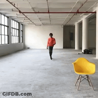A Man In An Orange Shirt Walks Through An Empty Room GIF