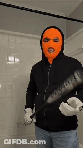 A Man In An Orange Ski Mask Is Holding A Bat GIF