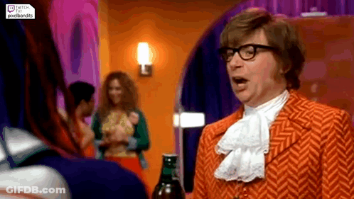 A Man In An Orange Suit And Glasses Is Standing In A Room Talking To A Woman . GIF
