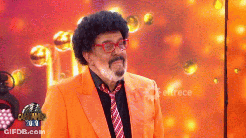 A Man In An Orange Suit And Tie Is Standing In Front Of A Sign That Says Cantando 2.0 GIF