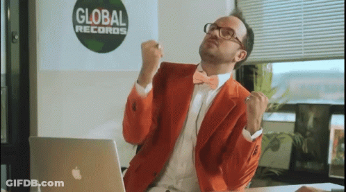 A Man In An Orange Suit Is Sitting In Front Of An Apple Laptop In Front Of A Global Records Sign GIF