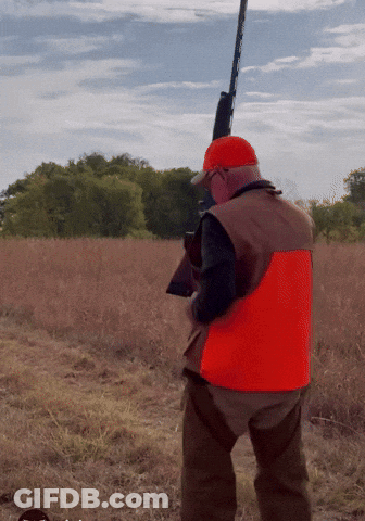 A Man In An Orange Vest Is Holding A Gun GIF