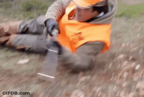 A Man In An Orange Vest Is Laying On The Ground With A Knife . GIF