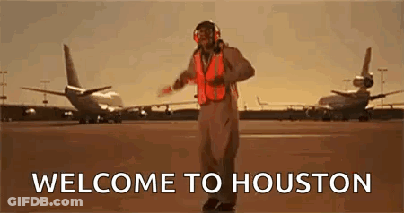 A Man In An Orange Vest Is Standing On A Runway In Front Of Planes . GIF