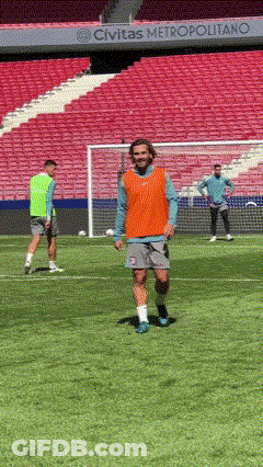 A Man In An Orange Vest Is Walking On A Soccer Field In Front Of A Sign That Says Civitas Metropolitano GIF