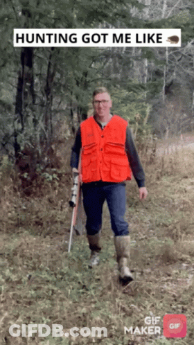 A Man In An Orange Vest Is Walking Through The Woods With A Rifle GIF