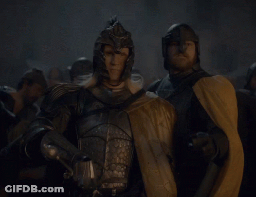 A Man In Armor Holding A Sword Stands Next To Another Man GIF
