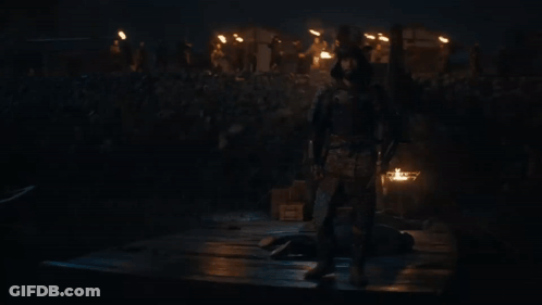 A Man In Armor Stands In Front Of A Crowd Of People Holding A Sword GIF