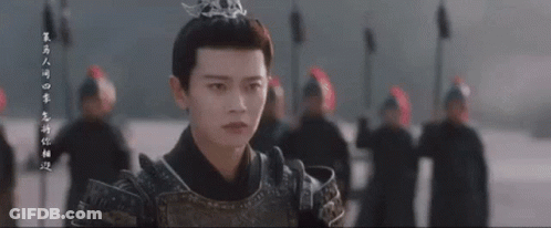 A Man In Armor With A Crown On His Head Is Standing In Front Of A Group Of People . GIF