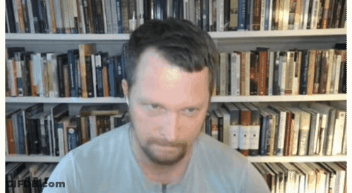 A Man In Front Of A Bookshelf With A Book Titled ' A Brief History ' On It GIF