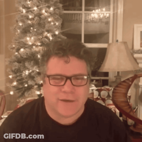 A Man In Front Of A Christmas Tree Wearing Glasses GIF