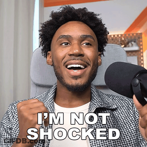 A Man In Front Of A Microphone With The Words I 'M Not Shocked Above Him GIF