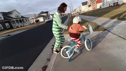 A Man In Green And White Striped Pajamas Helps A Little Girl Ride A Bike GIF