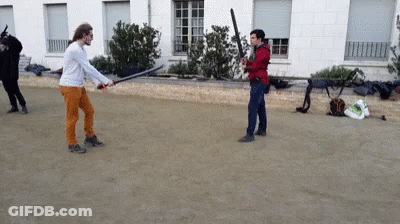 A Man In Orange Pants Is Holding A Sword While Another Man Holds A Bat GIF