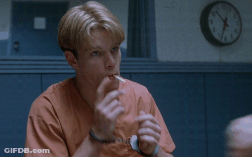 A Man In Orange Scrubs Is Sitting In Front Of A Wall Clock That Says Sounds Like GIF