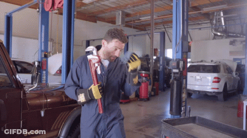 A Man In Overalls Is Holding A Wrench In Front Of A Jeep GIF
