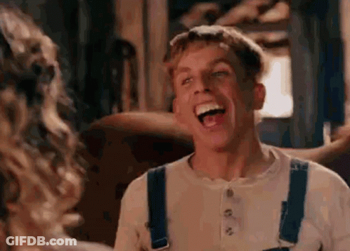 A Man In Overalls Is Laughing While Looking At A Woman In A Room . GIF