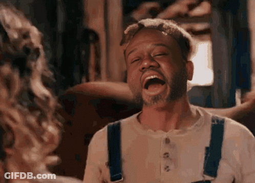 A Man In Overalls Is Laughing With His Mouth Wide Open . GIF