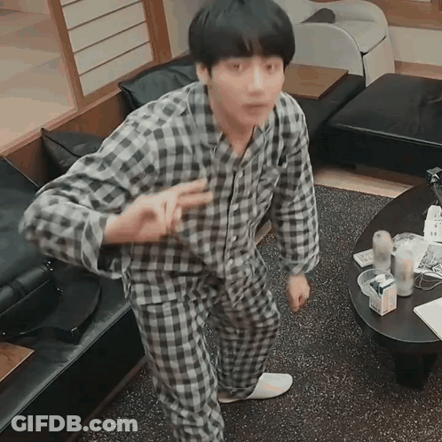 A Man In Plaid Pajamas Is Standing In A Living Room GIF