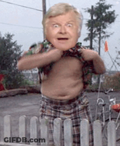 A Man In Plaid Shorts Is Standing Behind A Fence With His Shirt Off GIF