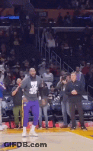 A Man In Purple Pants Is Standing On A Basketball Court In Front Of A Crowd Of People . GIF