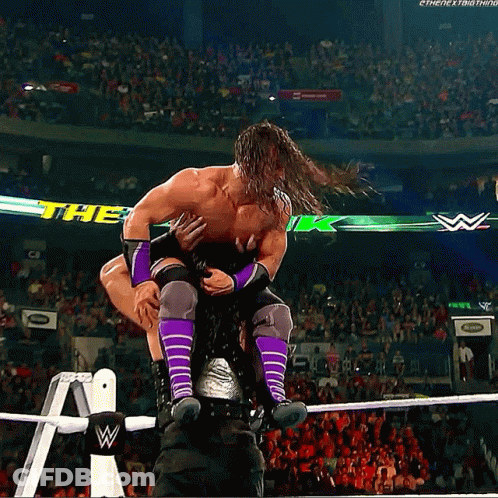 A Man In Purple Socks Is Being Lifted In The Air By Another Man GIF