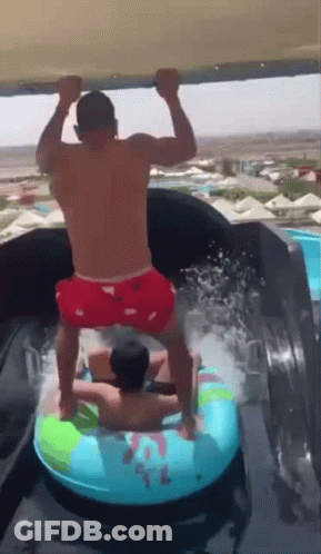 A Man In Red Shorts Is Standing On A Water Slide With Another Man GIF