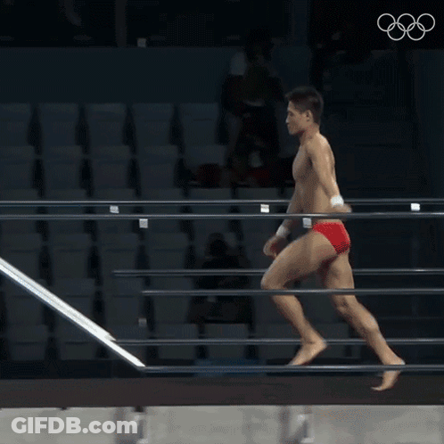 A Man In Red Swim Trunks Is Diving Into A Pool At The Olympics GIF