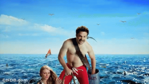A Man In Red Swim Trunks Is Standing In The Ocean GIF