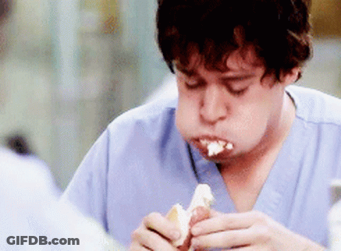A Man In Scrubs Is Eating A Hot Dog With Cream Cheese GIF