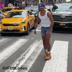 A Man In Shorts And A Tank Top Is Crossing A Street In Front Of A Yellow Car . GIF